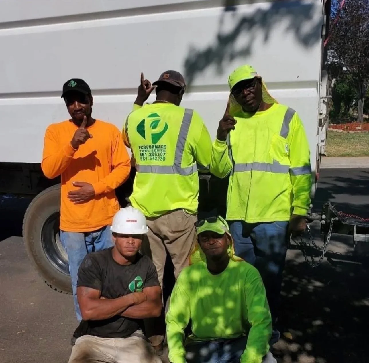 Five tree service crew members in safety vests and hard hats standing in front of service truck