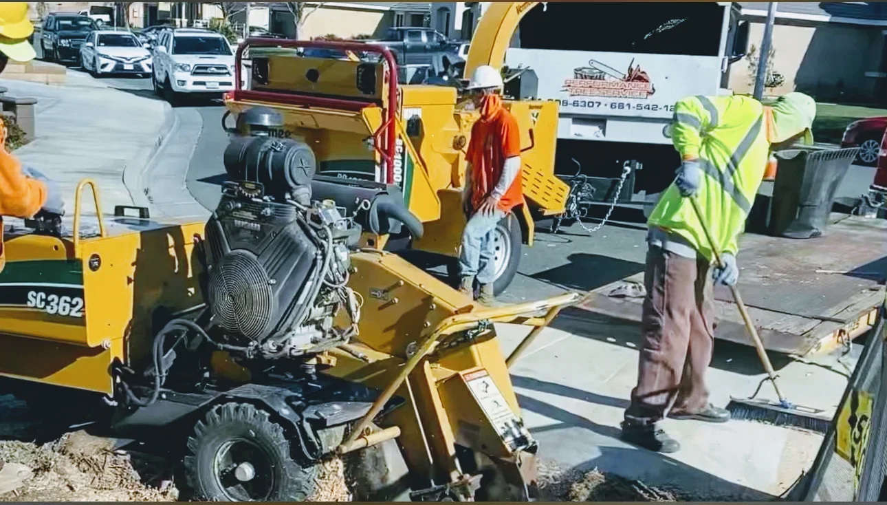 Yellow diesel chipper with engine and hydraulic system, crew in safety vests at equipment staging area